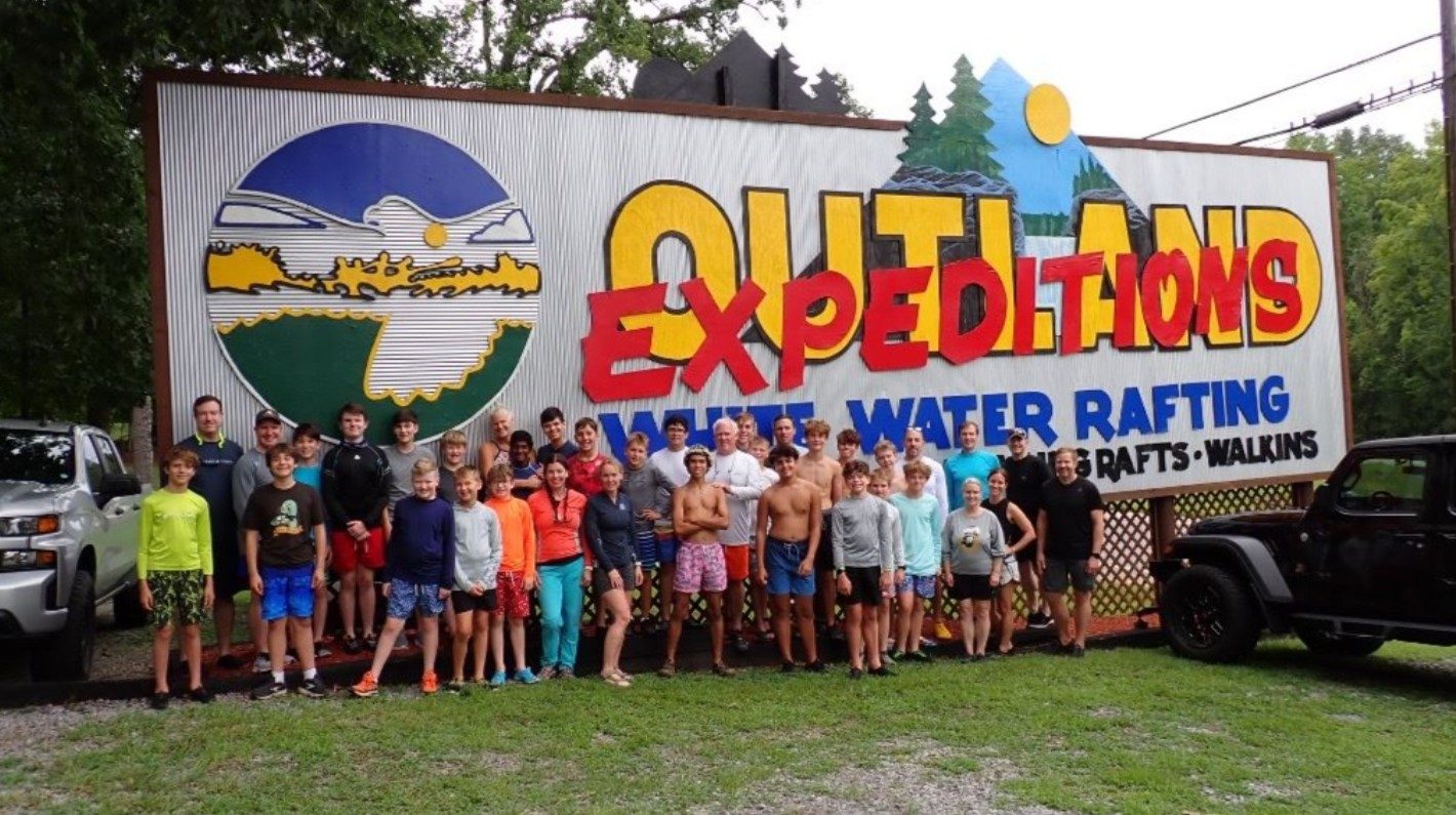 Troop 8 Scouts and adult leaders in front of the Outland Expeditions white water rafting sign